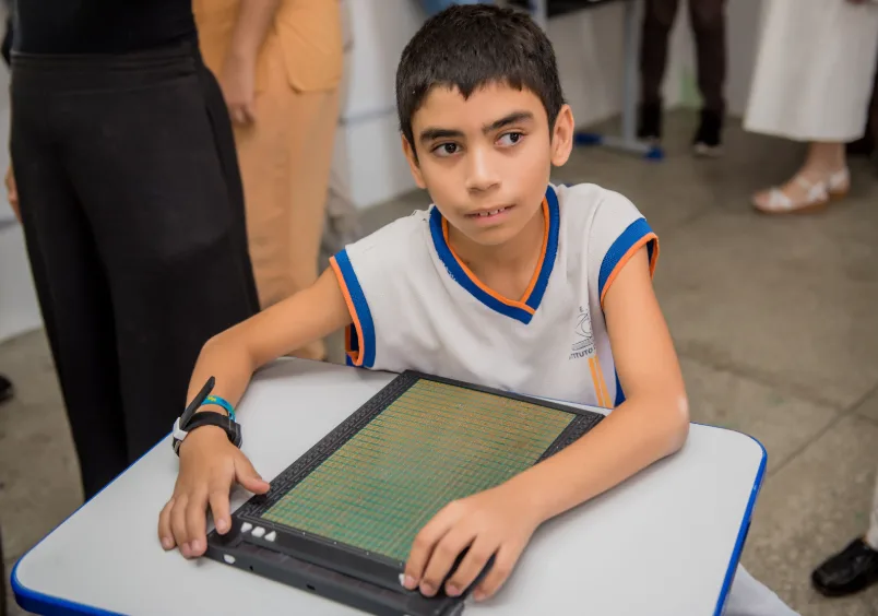 Estudante lendo e escrevendo na grade de pontos do NoteBraille